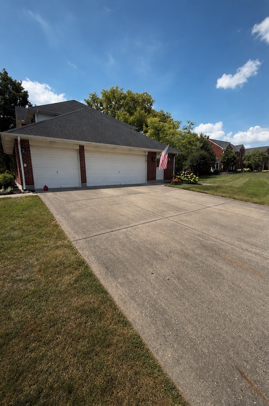 The same driveway before pressure washing, with dark buildup visible across the concrete